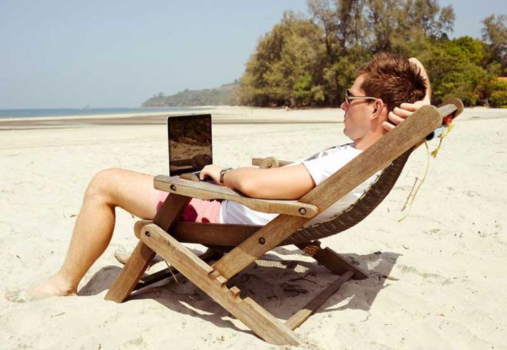 Man sat in deck chair with lap top on beach